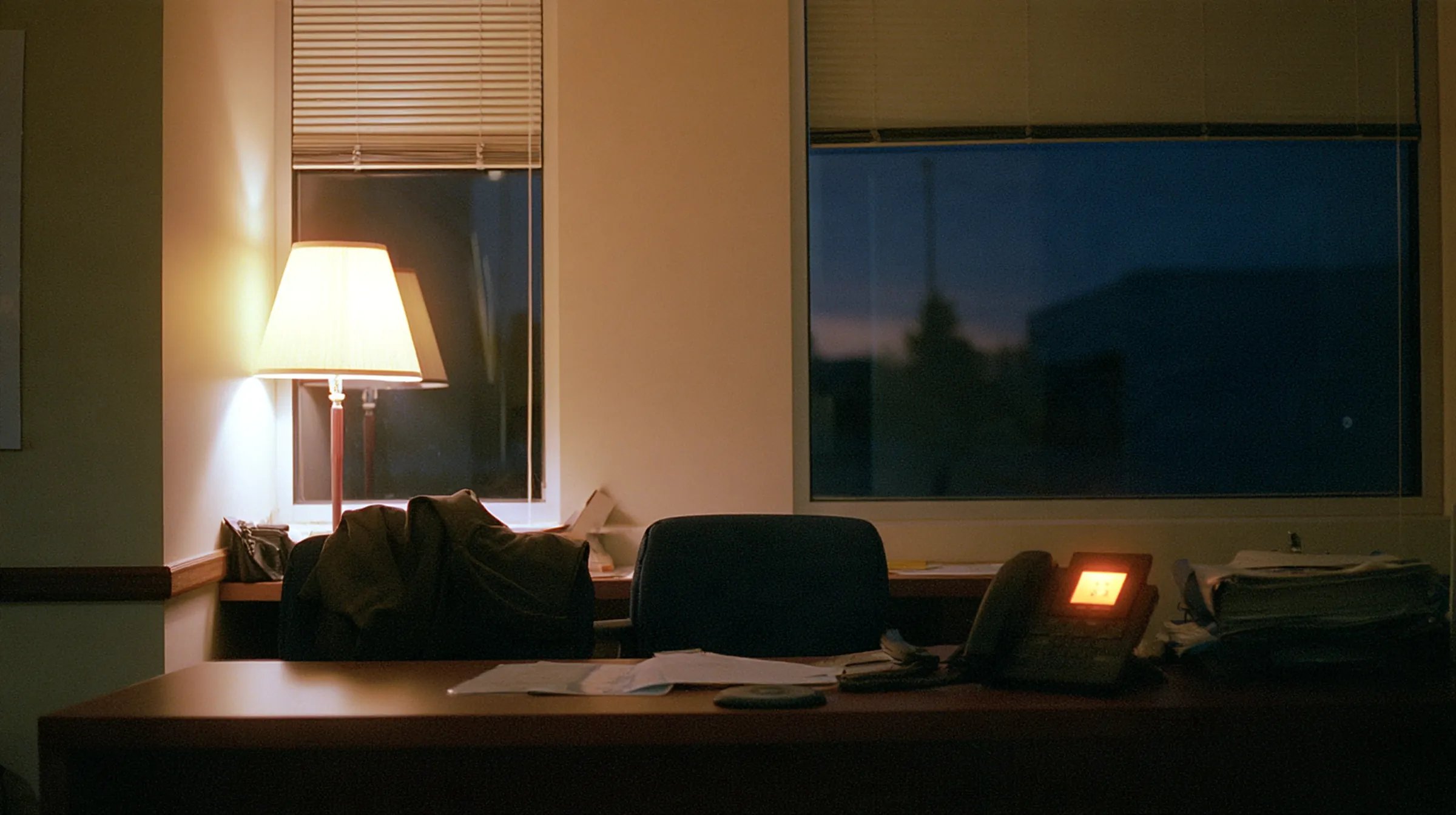 An empty front desk after closing, lamp on, the desk phone lit with an incoming call